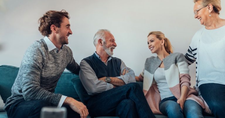 A younger adult man and an older adult man sit on a couch next to a younger adult woman and an older adult woman.